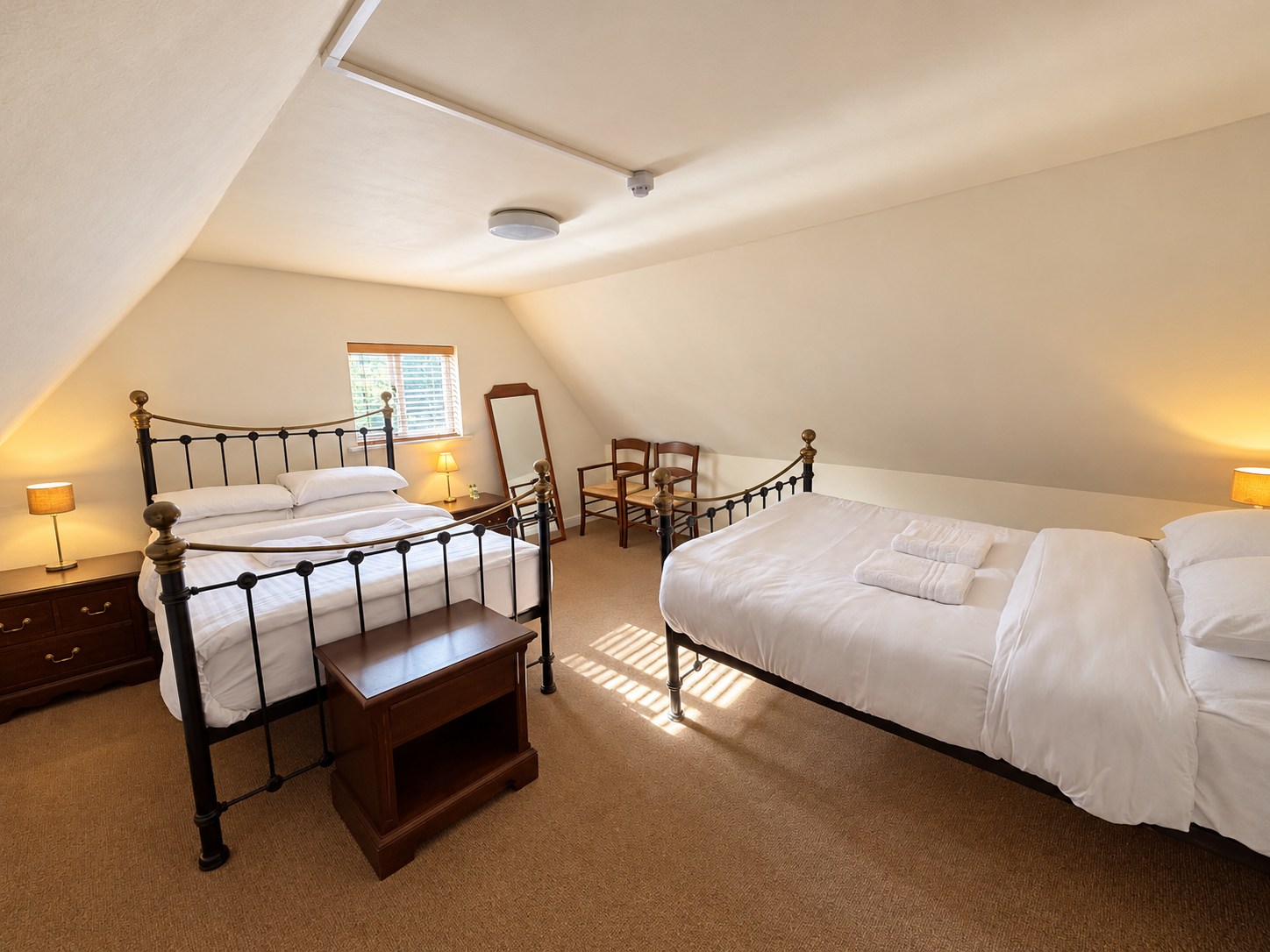 Bedroom Four with two iron double beds, white bedding and warm bedside lamps beneath a sloping ceiling