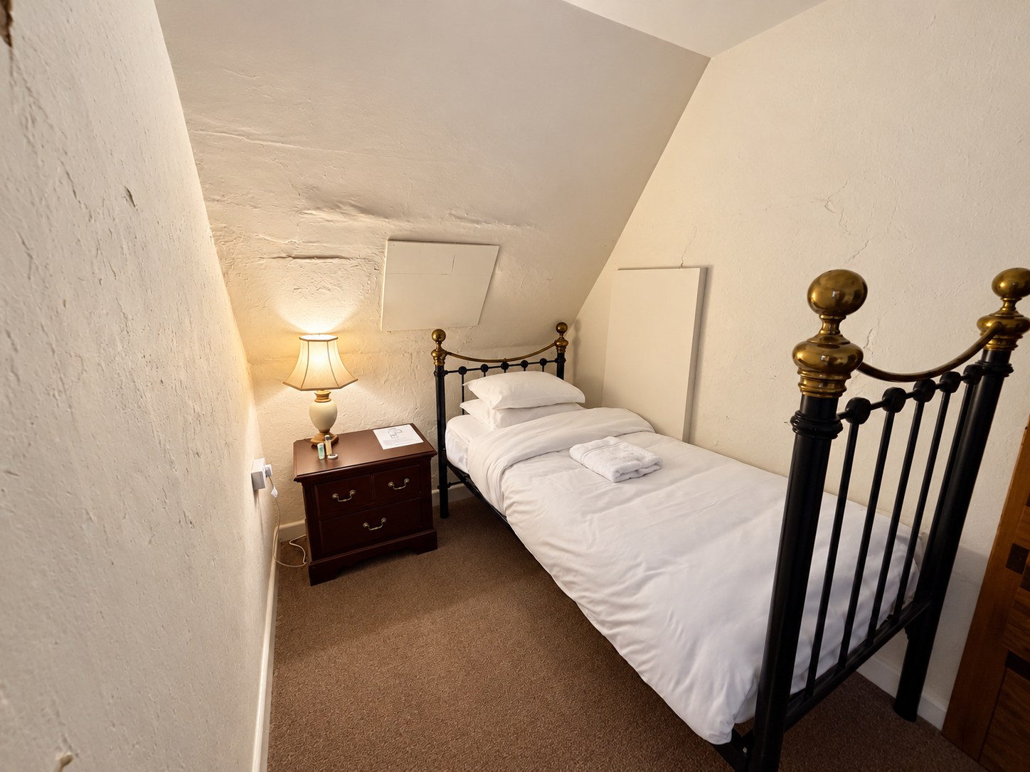 Bedroom Three with a single iron bed, white bedding and a bedside lamp beneath a sloping ceiling