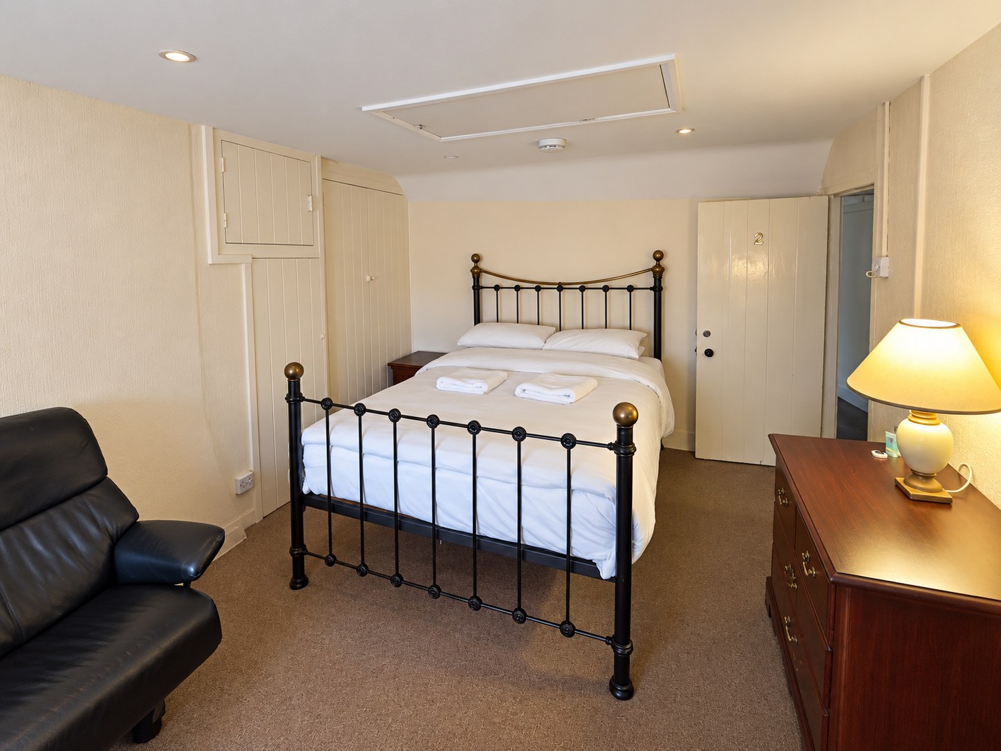 Bedroom Two with an iron bed, white bedding, a black armchair and a warm table lamp